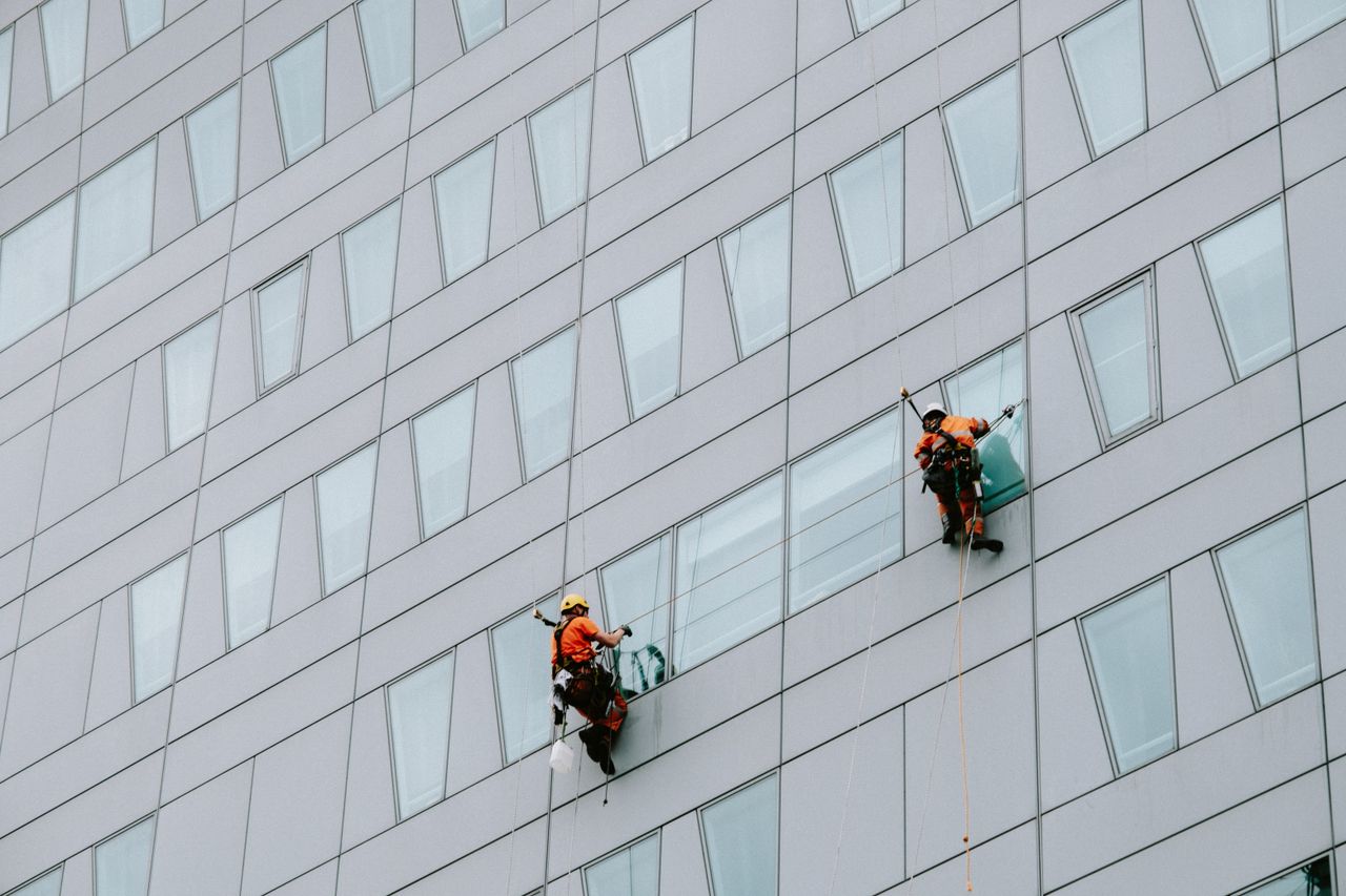 team-03 High-rise window washers in safety gear cleaning a skyscraper facade.