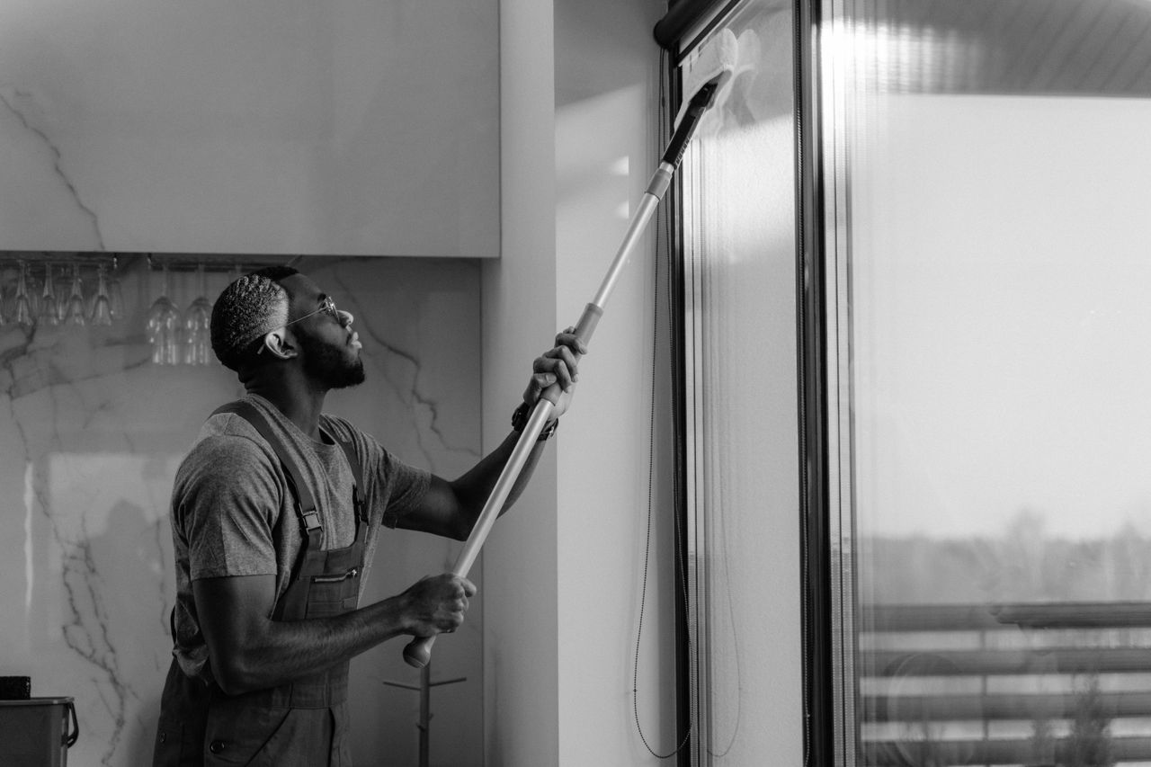 services-04 A man cleaning a glass window with a mop in grayscale, showcasing professional work.