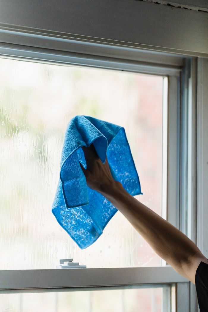 who-we-are A hand using a blue towel to clean a window indoors, showcasing housework.