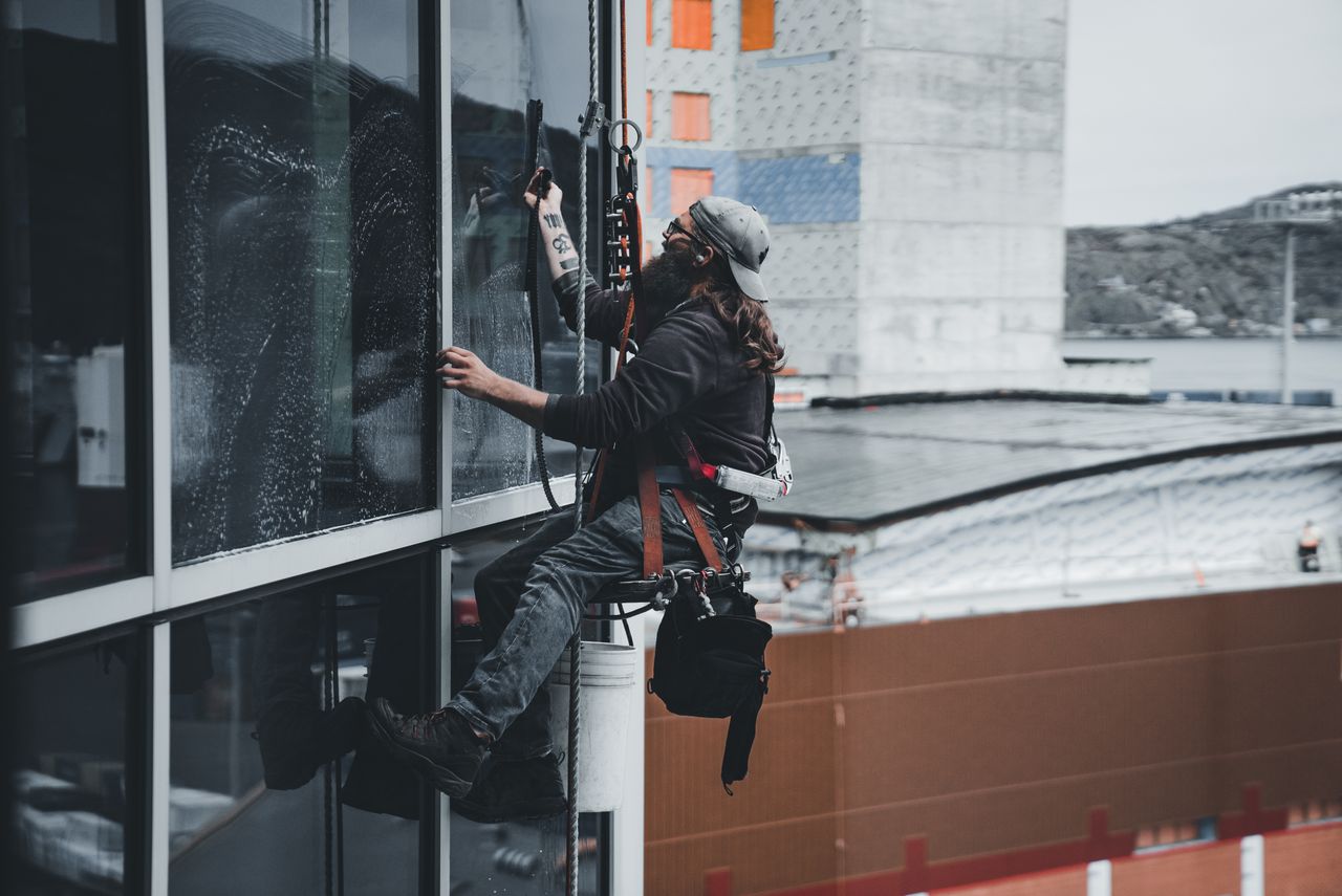 team-01 A man cleaning skyscraper windows with a harness, showcasing urban high-rise work.