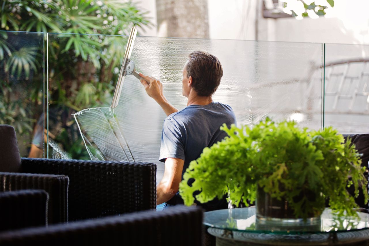 why-choose-us A man cleaning a glass barrier outdoors with a squeegee, surrounded by greenery.